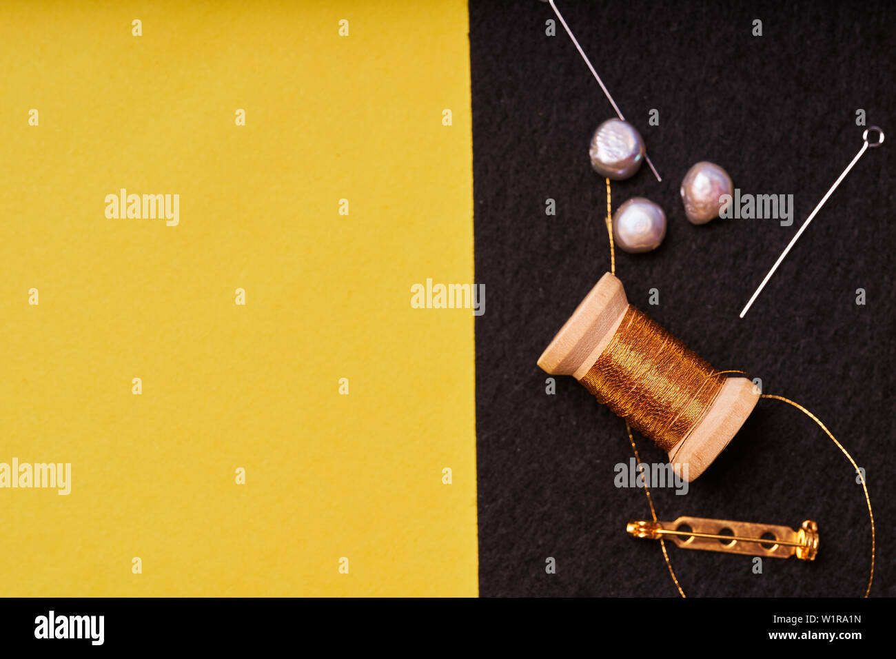 Embroidery products and tools. Coil metal threads, pearls and a pin with the needle on the black felt. Stock Photo