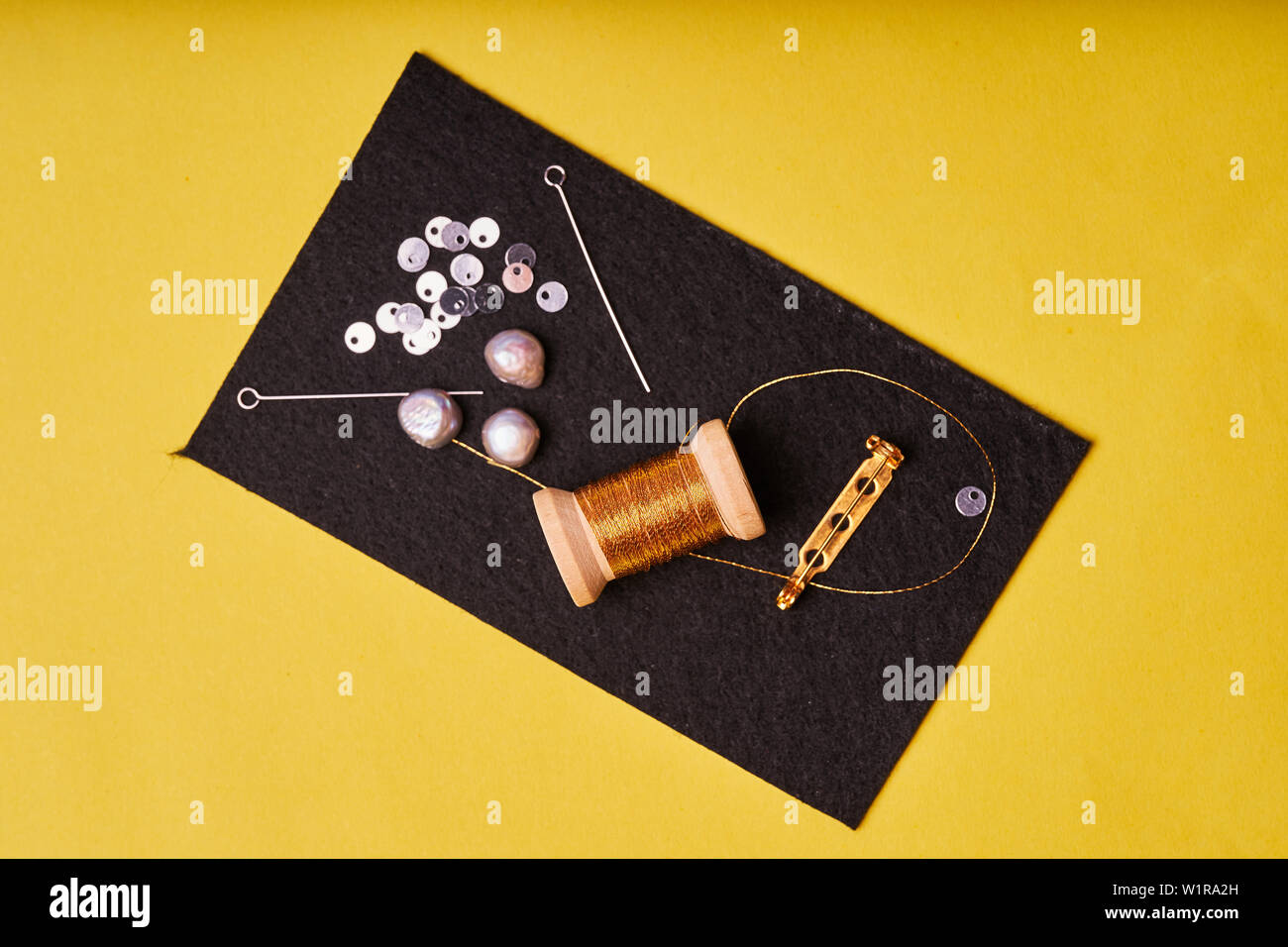 Embroidery products and tools. Coil metal threads, pearls and a pin with the needle on the black felt. Stock Photo