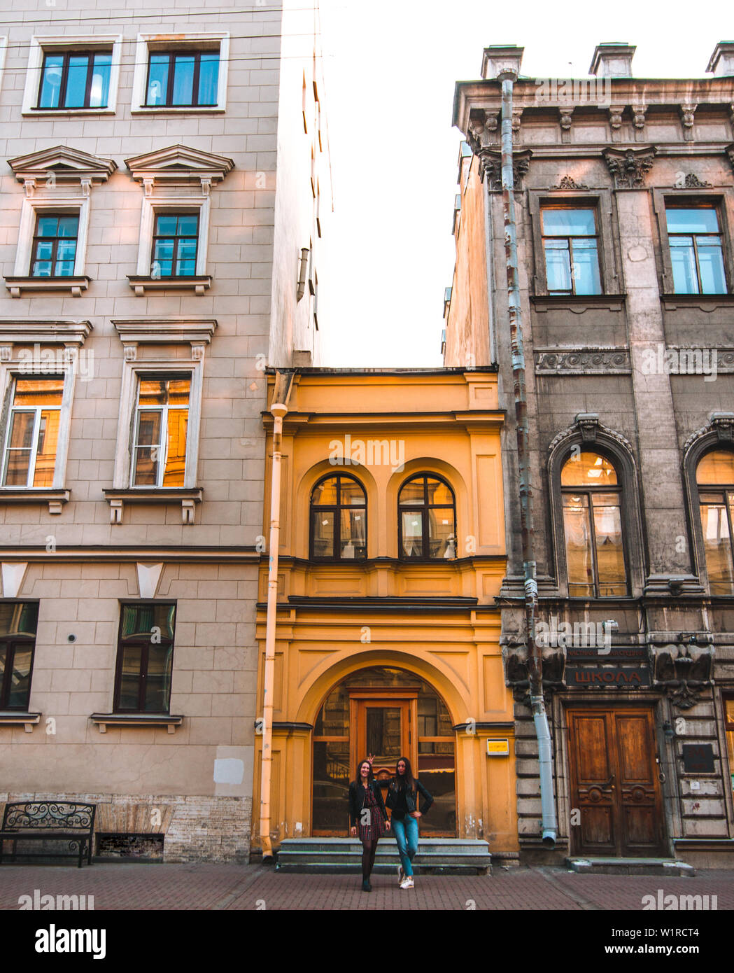 Two attractive girls stand near beautiful old European buildings on a sunny day in St. Petersburg. yellow bright building. Stock Photo
