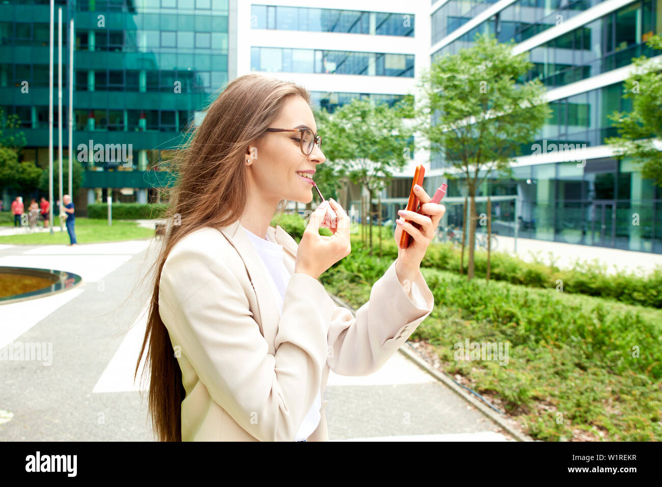 Shot of young woman applying lipstick while standing on the street. Stock Photo