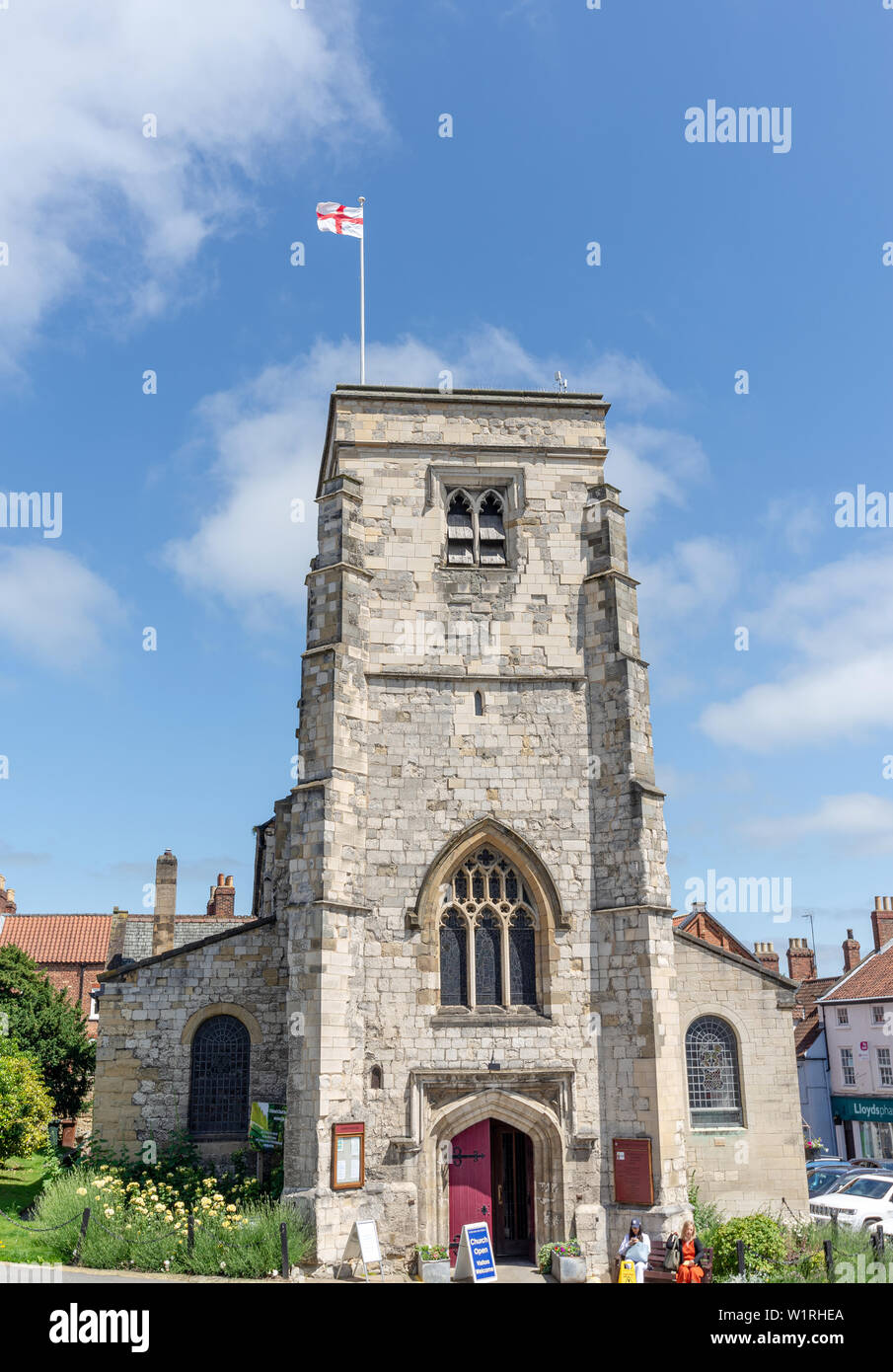 St Michael’s Church, Malton.  The church has buildings to the side and rear and a flag flies from the tower.  A blue sky is above. Stock Photo