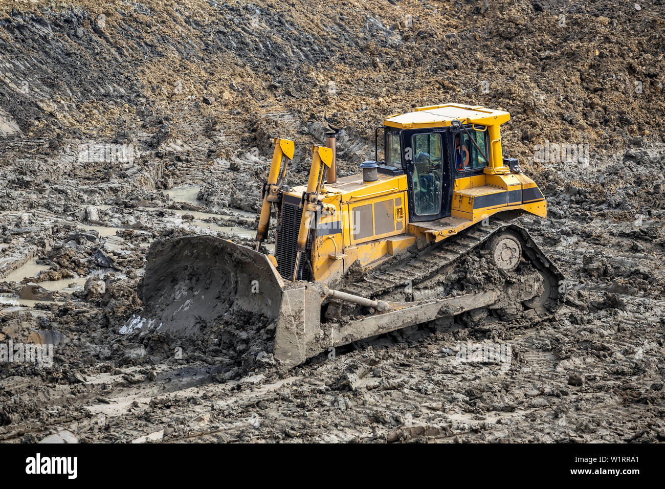 Yellow dozer pushes large piles of dirt on a construction site Stock