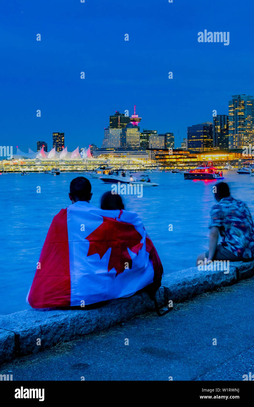 Couple wrapped in Canadian flag wait for Canada Day Fireworks, Stanley Park, Vancouver, British Columbia, Canada Stock Photo