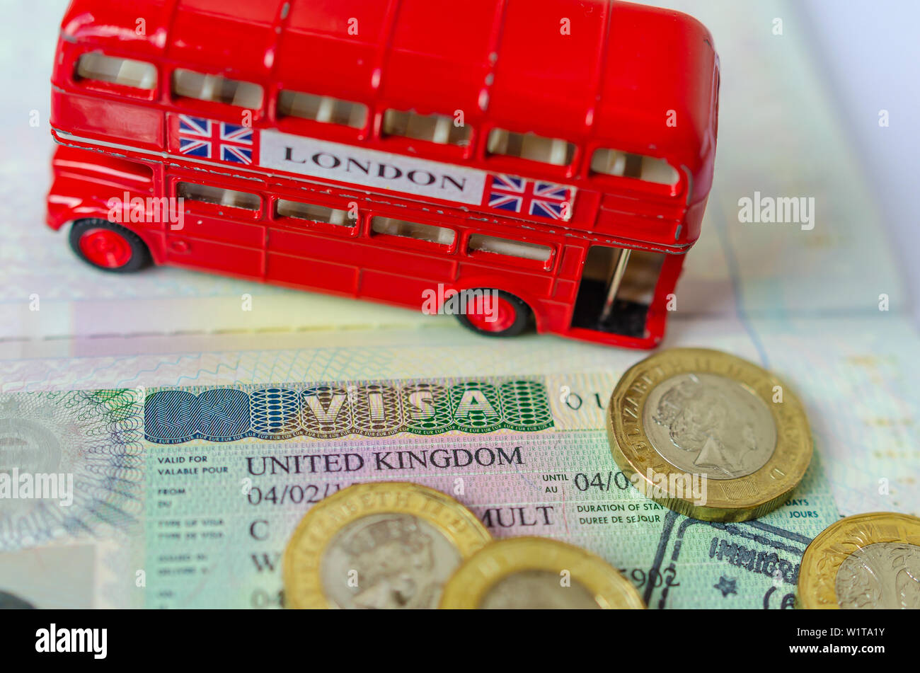 UK visa sticker in a passport surrounded by pound coins and double-decker bus model. Concept for travel and holiday. Stock Photo
