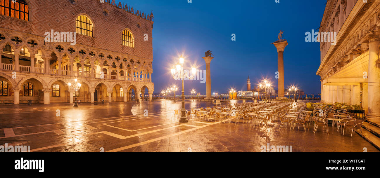 Panorama of St. Mark's Square with the illuminated facade of the Doge's Palace, lanterns and columns with Markus Lion and the San Todaro statue in blu Stock Photo