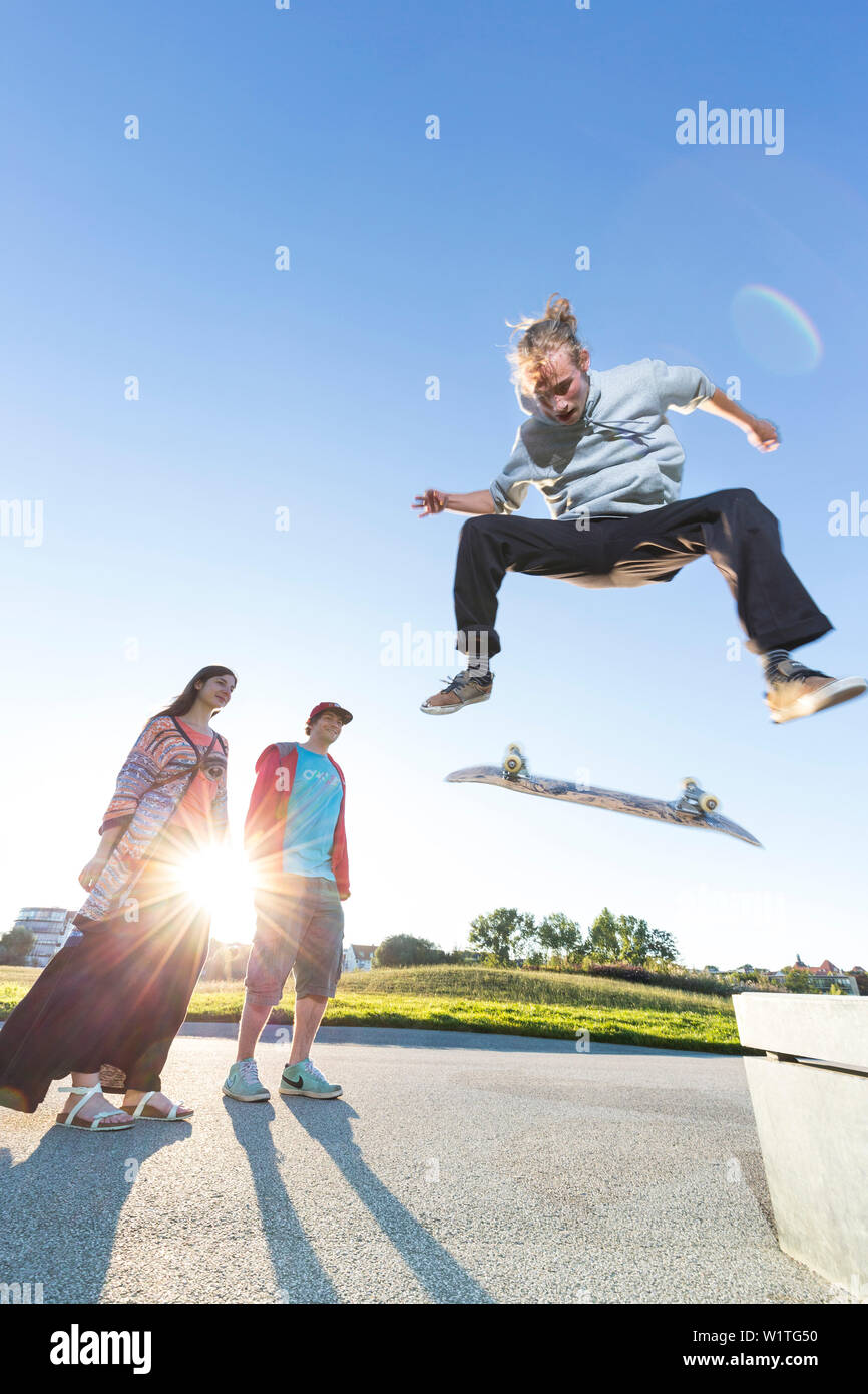 Skater jumping with his skateboard from bench, kickflip, ollie, sunset, hipster, swimming meadow, provincial capital, Mecklenburg lakes, Schwerin, Mec Stock Photo