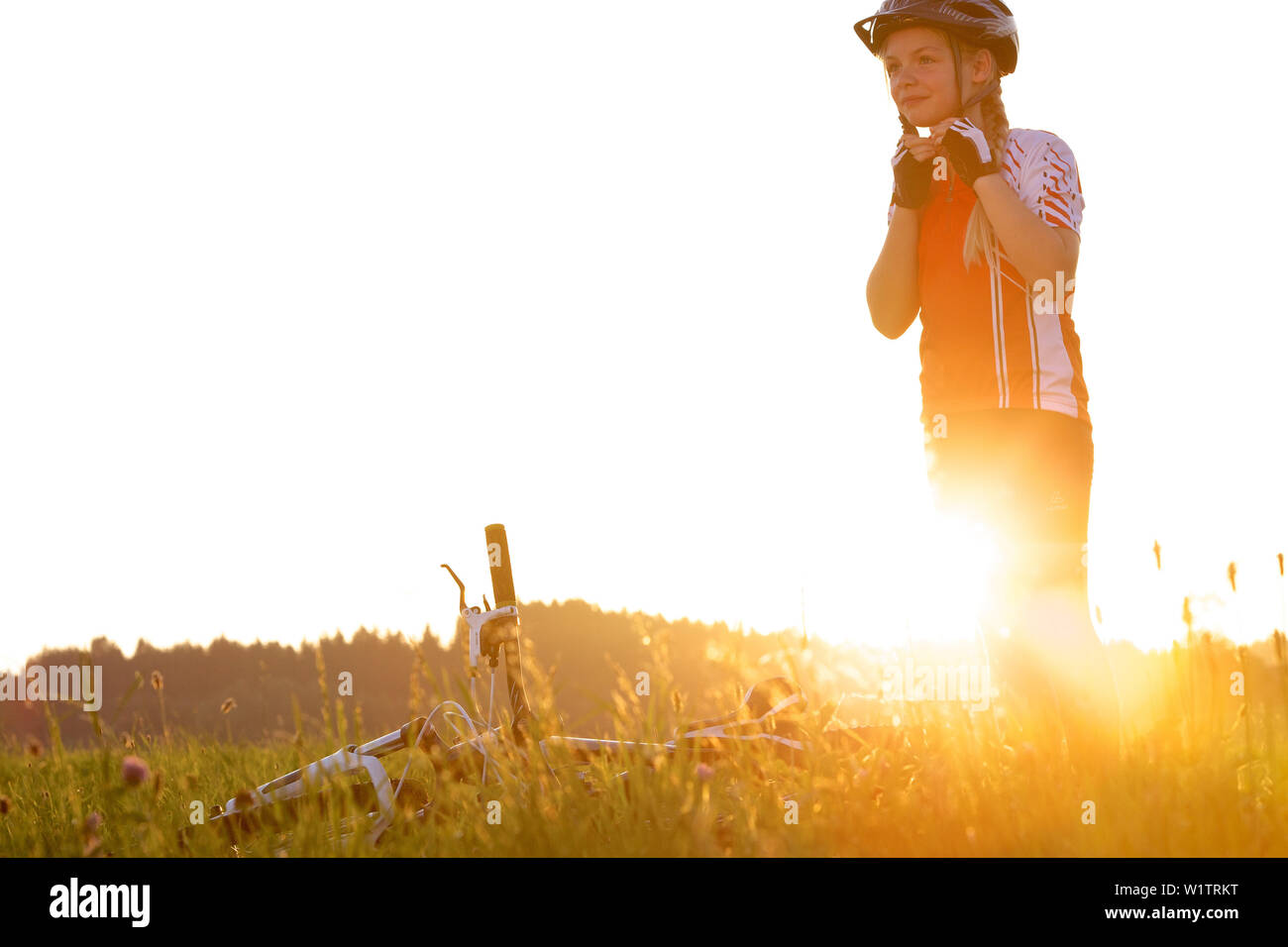 girl putting on her bicyle helmet on a meadow, Fuessen, Bavaria, Germany Stock Photo