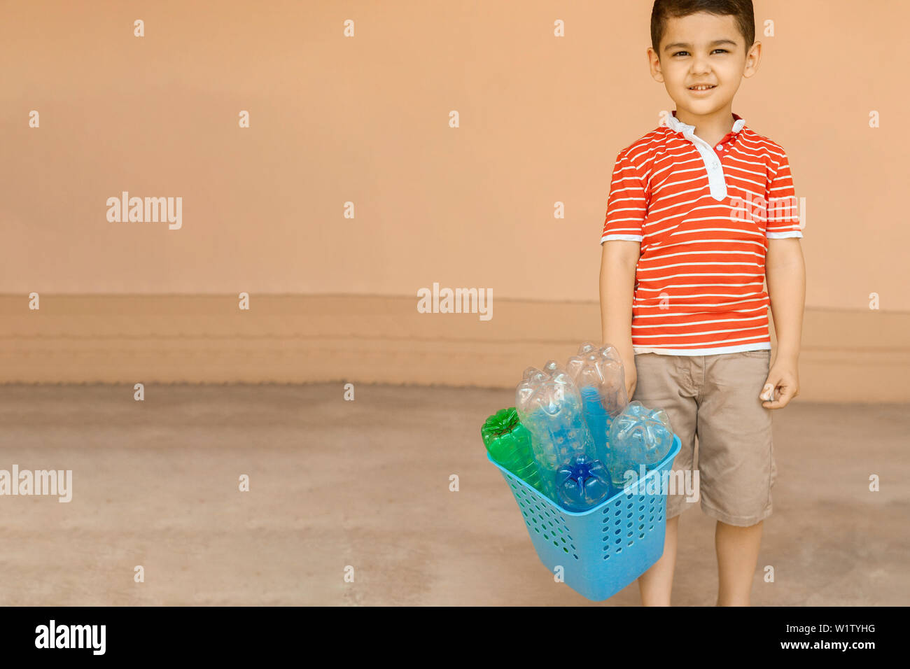 Young boy (6-8) holding an armful of recyclable plastic bottles