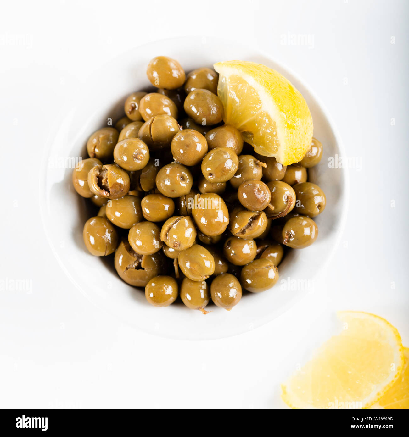 Green olives in bowl with lemon on white background. Green olives from