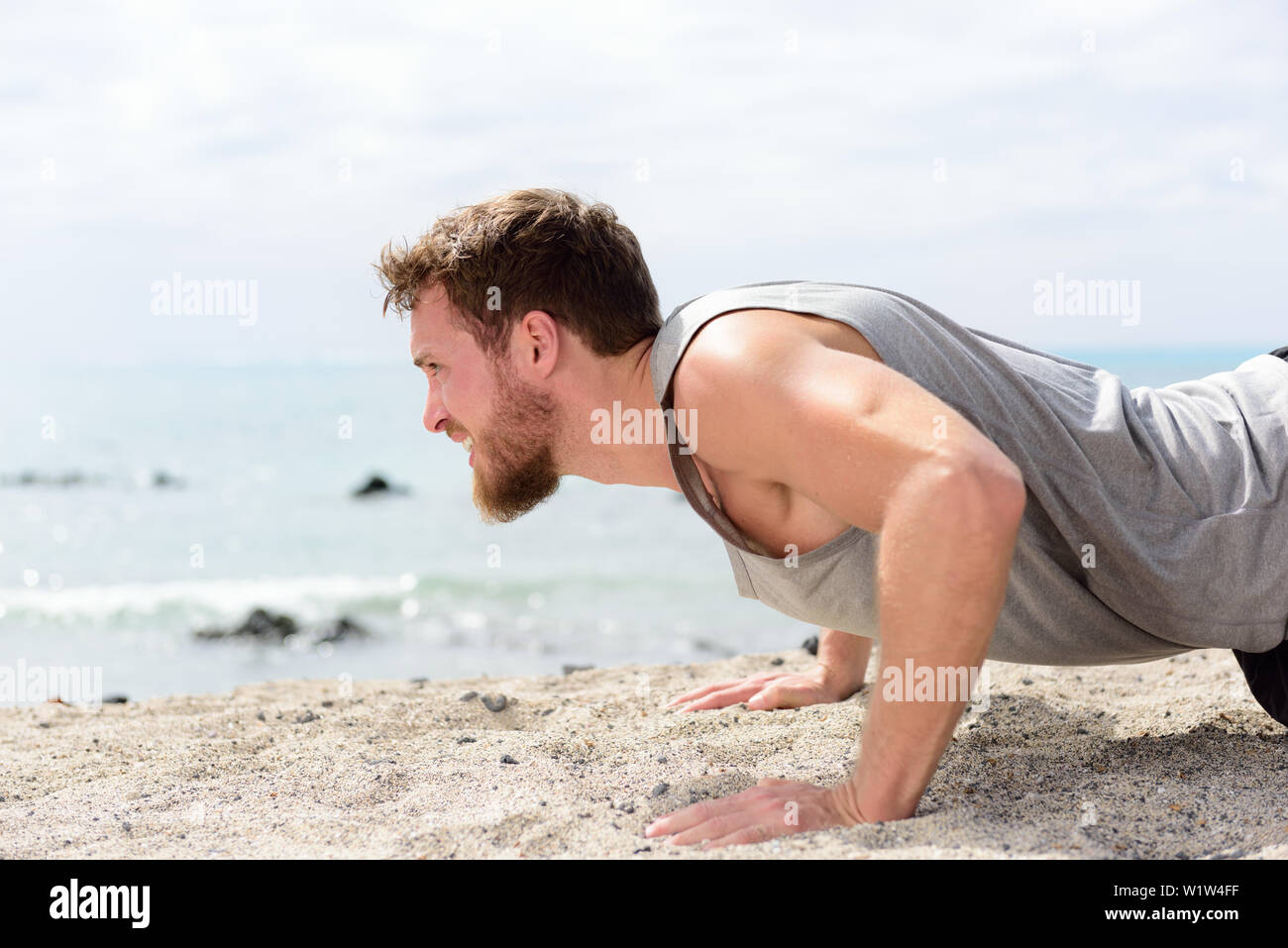 Fitness man doing pushup exercise on beach. Portrait of fit guy working out his arm muscles and