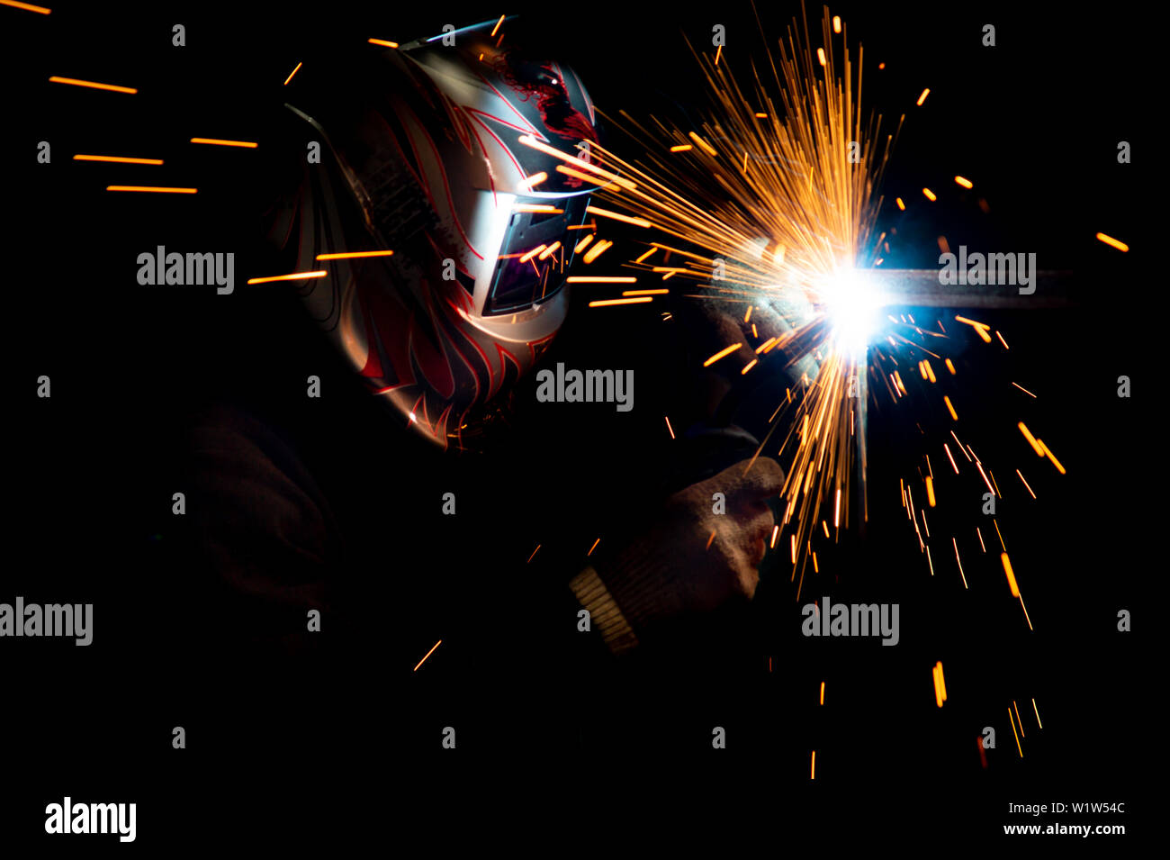 male welder in a mask performing metal welding. photo in dark colors. sparks flying. Stock Photo