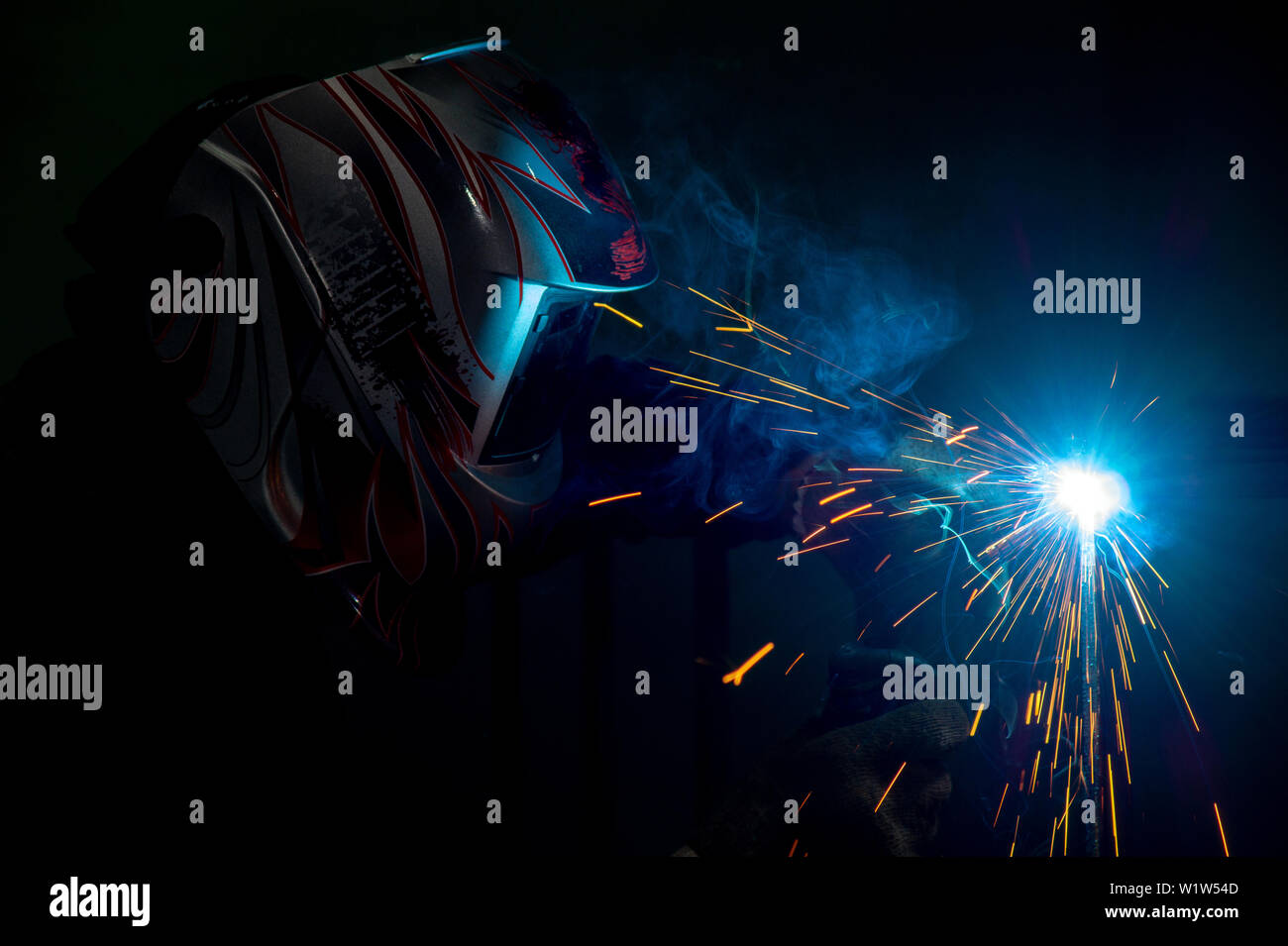 male welder in a mask performing metal welding. photo in dark colors. sparks flying. Stock Photo
