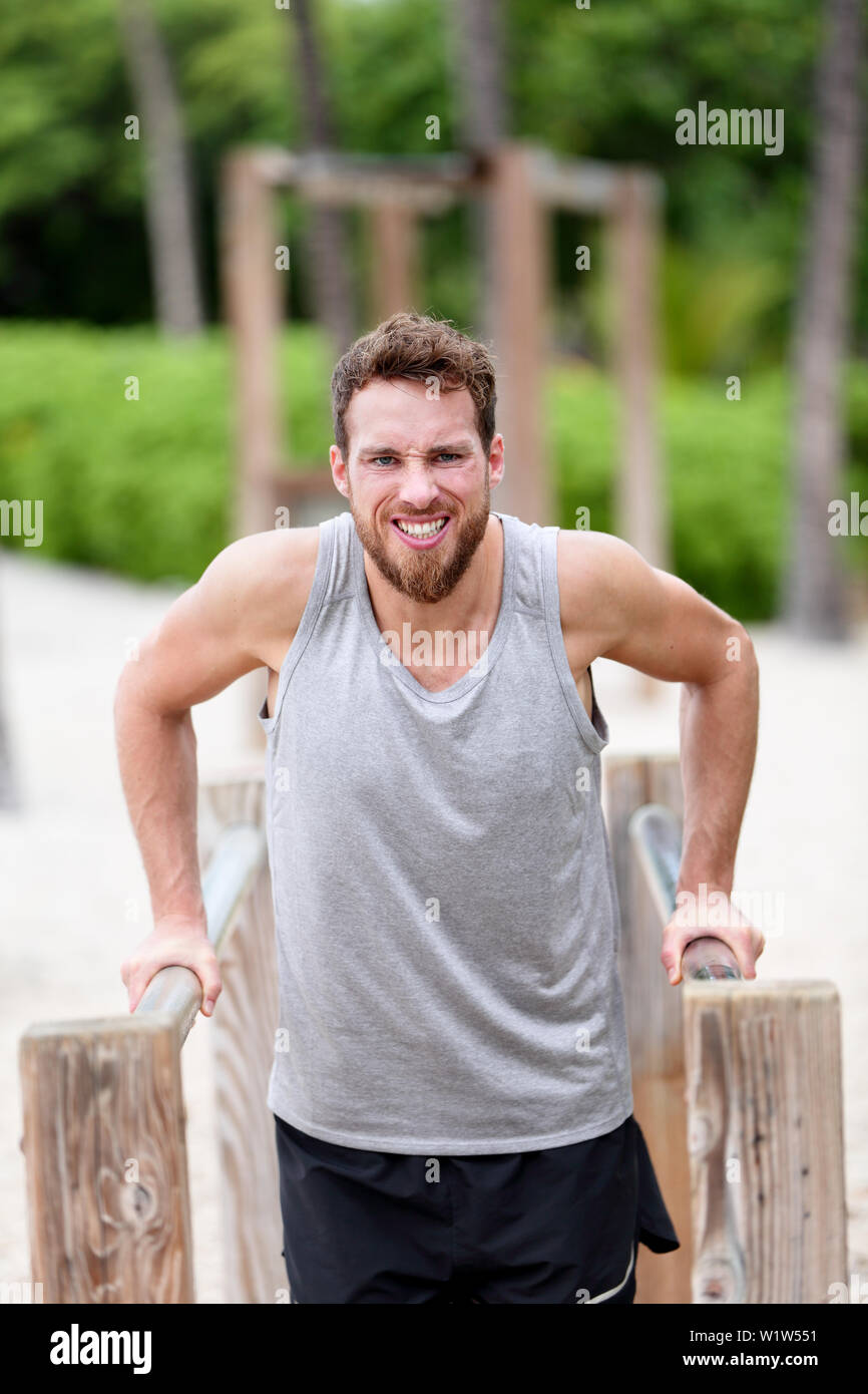 Man doing difficult strength training exercises - fitness cardio workout. Young Caucasian male athlete working out hard on outdoor jungle gym / monkey bars on summer beach Stock Photo