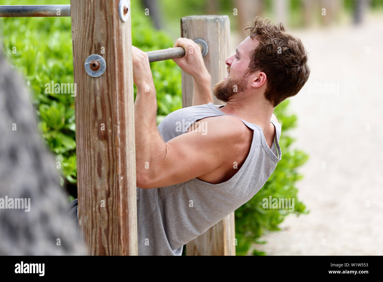 Pull-up strength training exercise - fitness man working out his arm muscles on outdoor beach gym doing chin-ups / pull-ups as part of a crossfit workout routine. Stock Photo