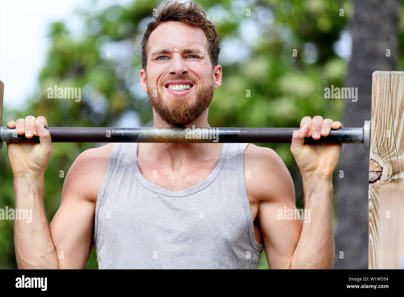 Crossfit fitness man exercising chin-ups workout. Young male adult trainer athlete portrait closeup with hands holding on monkey bars at outdoor gym doing a chin-up strength training muscle exercise. Stock Photo