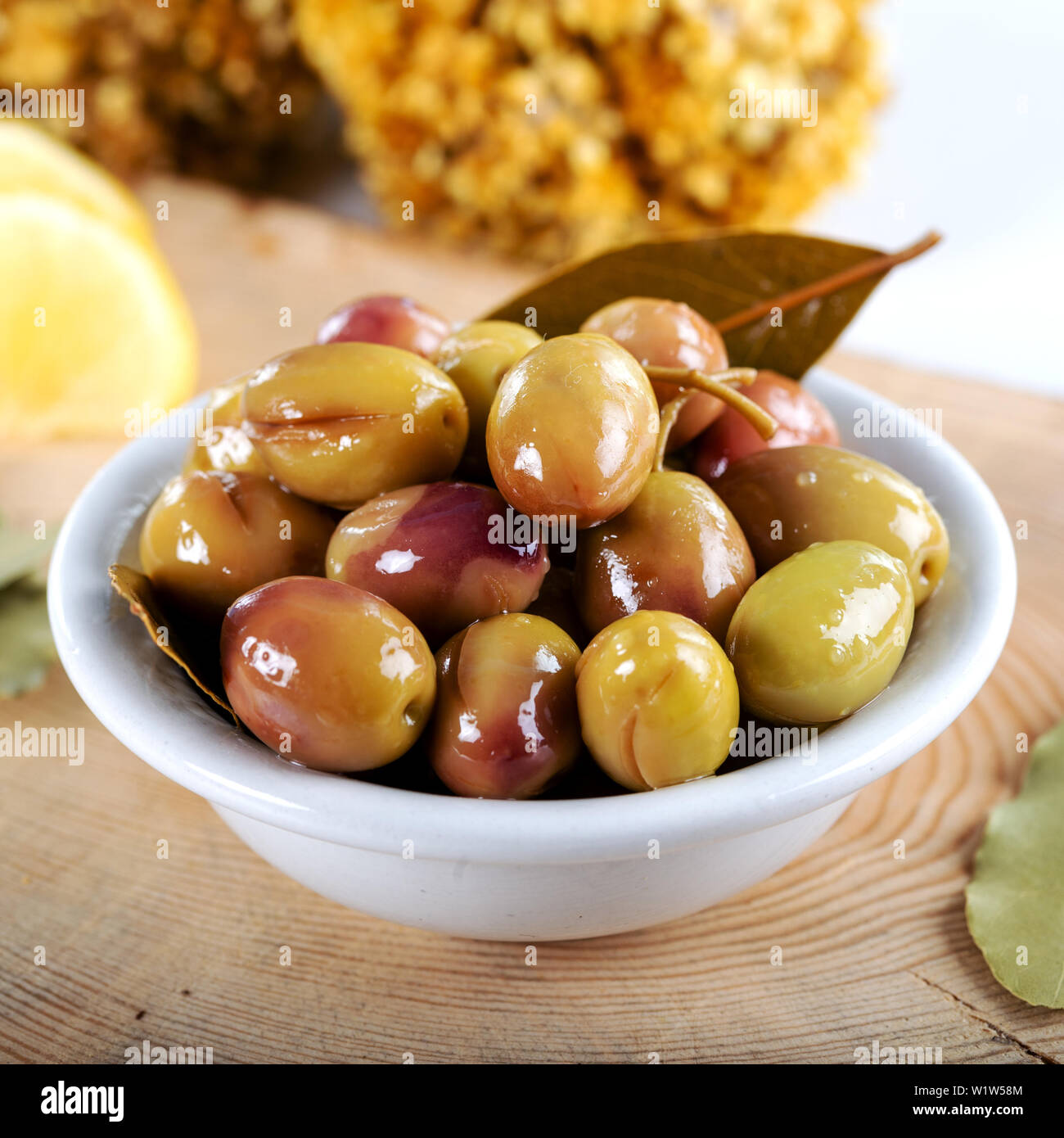 Green olives in bowl with lemons and daphne leaves. Stock Photo