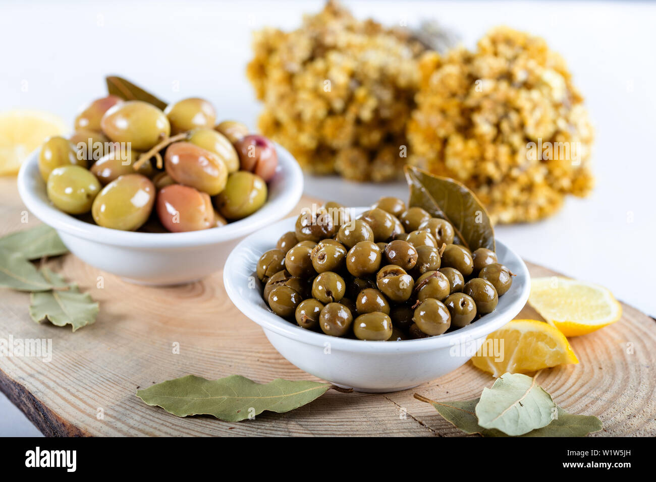 Green olives in bowl with lemons and daphne leaves. Stock Photo