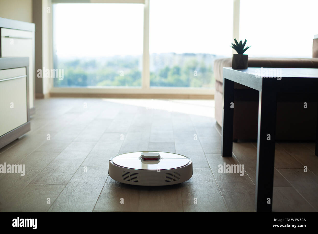 Smart House. Vacuum cleaner robot runs on wood floor in a living room ...