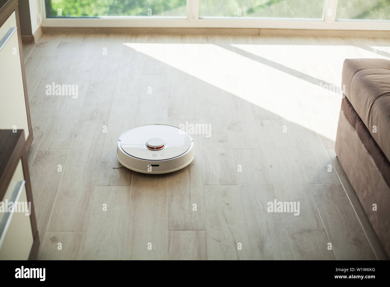 Smart House. Vacuum cleaner robot runs on wood floor in a living room ...