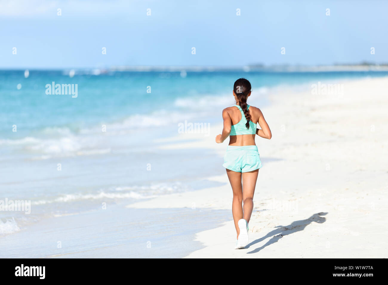 Sporty runner in running outfit training cardio jogging on sunny beach.  Unrecognizable person exercising legs and body on white sand next to ocean  waves Stock Photo - Alamy