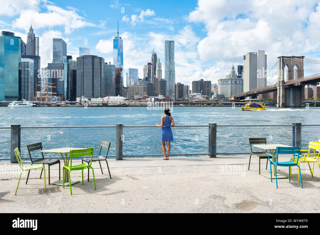 New York city skyline waterfront lifestyle - American people walking enjoying view of Manhattan over the Hudson river from the Brooklyn side. NYC cityscape with a public boardwalk with tables. Stock Photo
