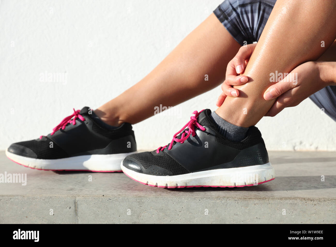 Ankle jogging injury female runner holding painful sprained ankle. Legs and  running shoes closeup of woman hands gripping on leg in pain because of  sore and injured joint and muscles in ankles