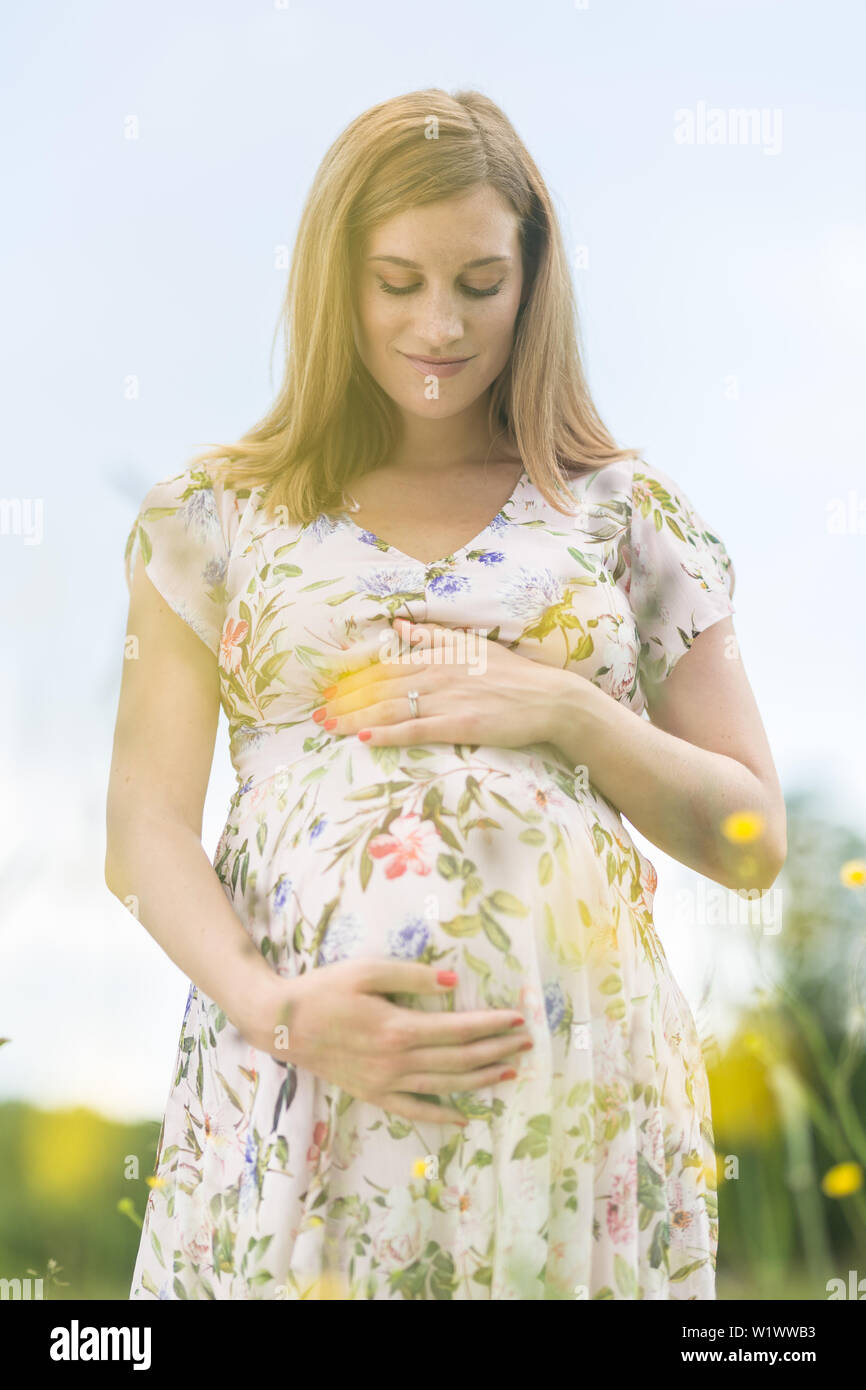 Beautiful pregnant woman in white summer dress in meadow full of yellow