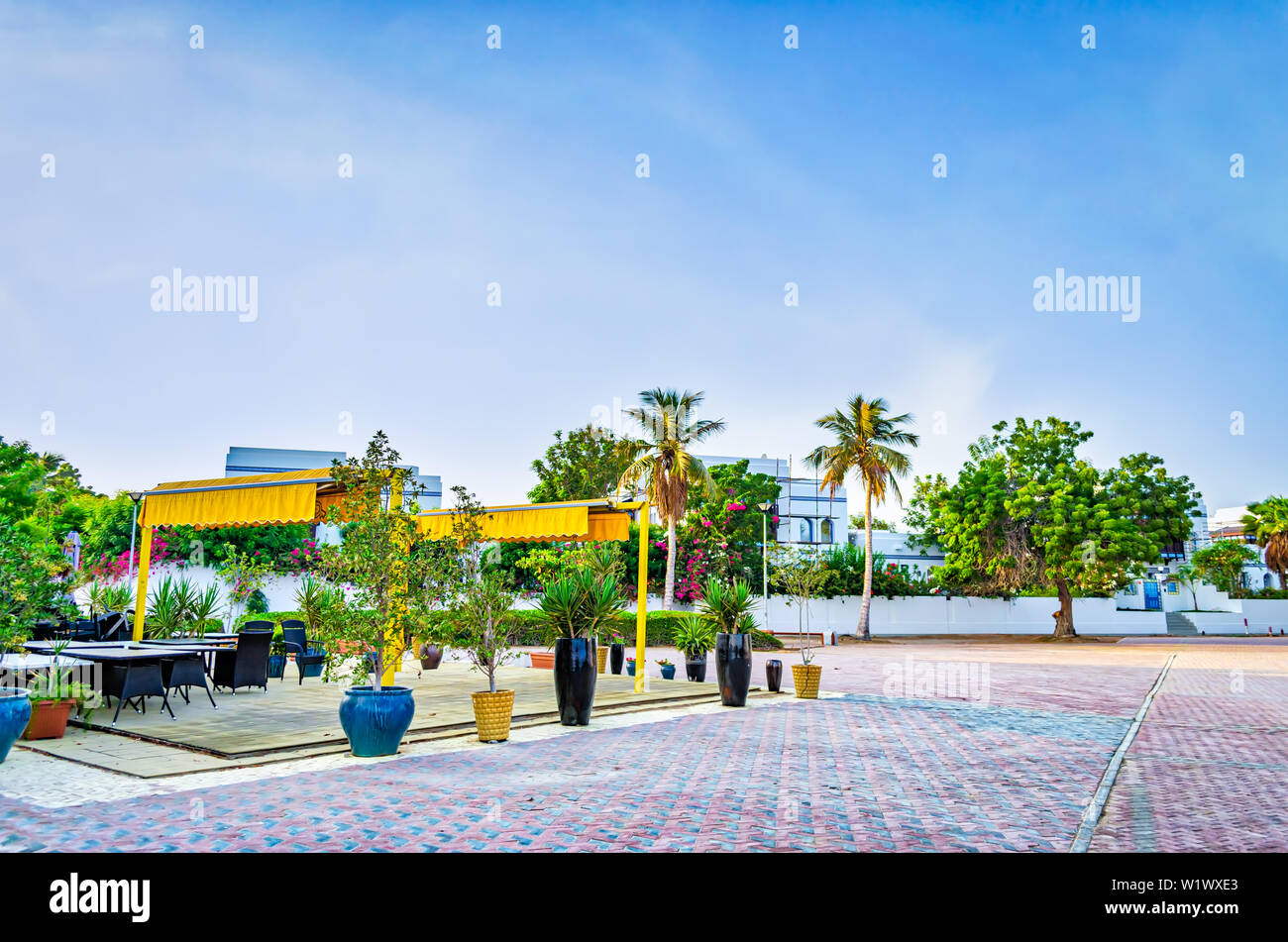 Small beach restaurant in yellow shades on the pavement surrounded by greenery. From Muscat, Oman. Stock Photo