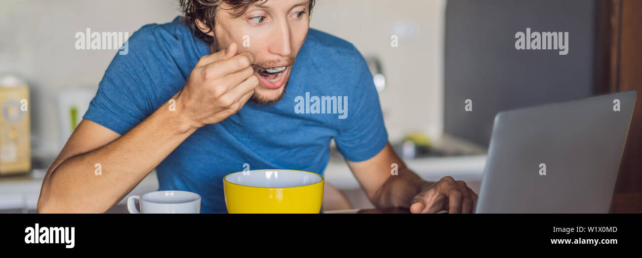 Young man having breakfast and using laptop on the kitchen BANNER, LONG FORMAT Stock Photo