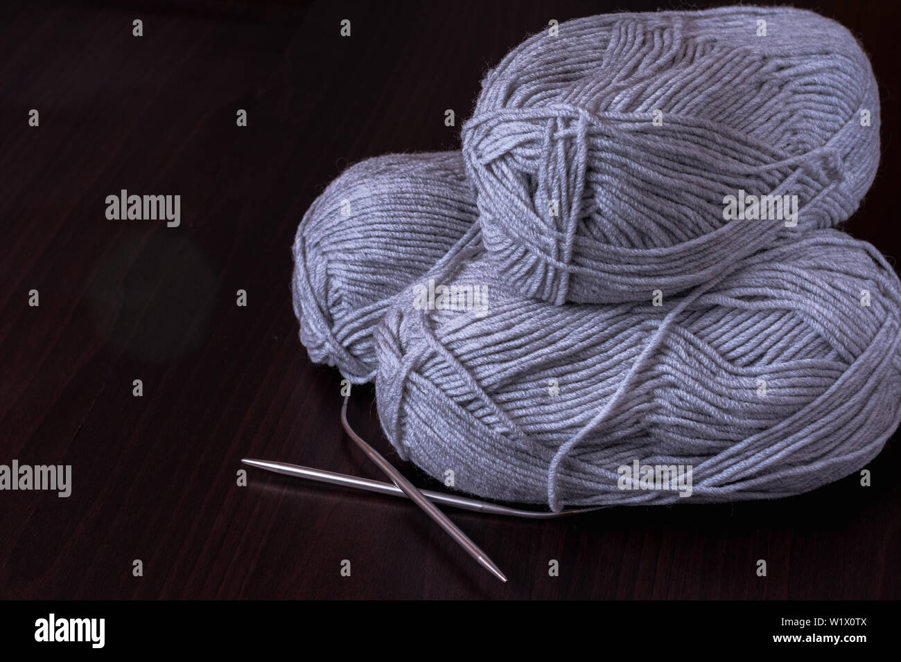 Hobbies and creative activities concept - three skeins of gray yarn with metal circular knitting needles on a wooden surface, selective focus, dark ke Stock Photo