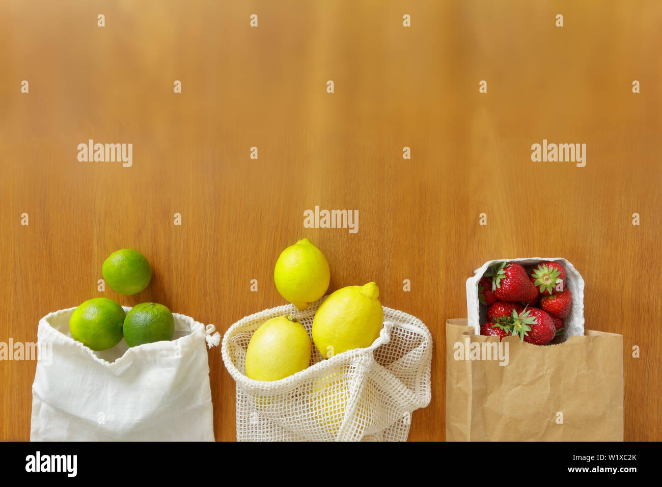 Cotton and paper reusable grocery bags with fresh fruits on wooden background, zero waste concept. Stock Photo