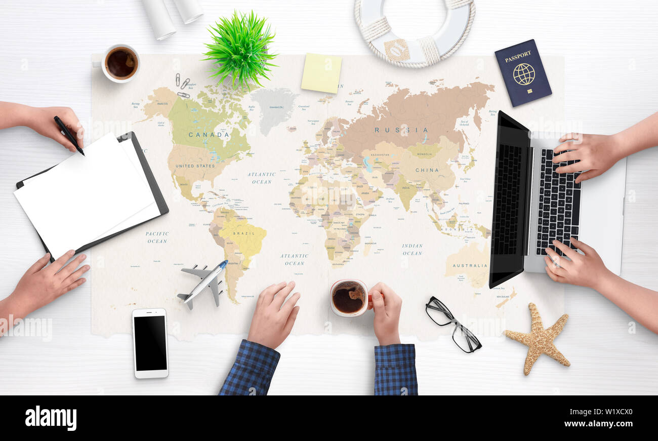 People are planning a holiday trip. Top view of the working tourist agency desk with a large world map in the background. Laptop, passport, papers, ph Stock Photo