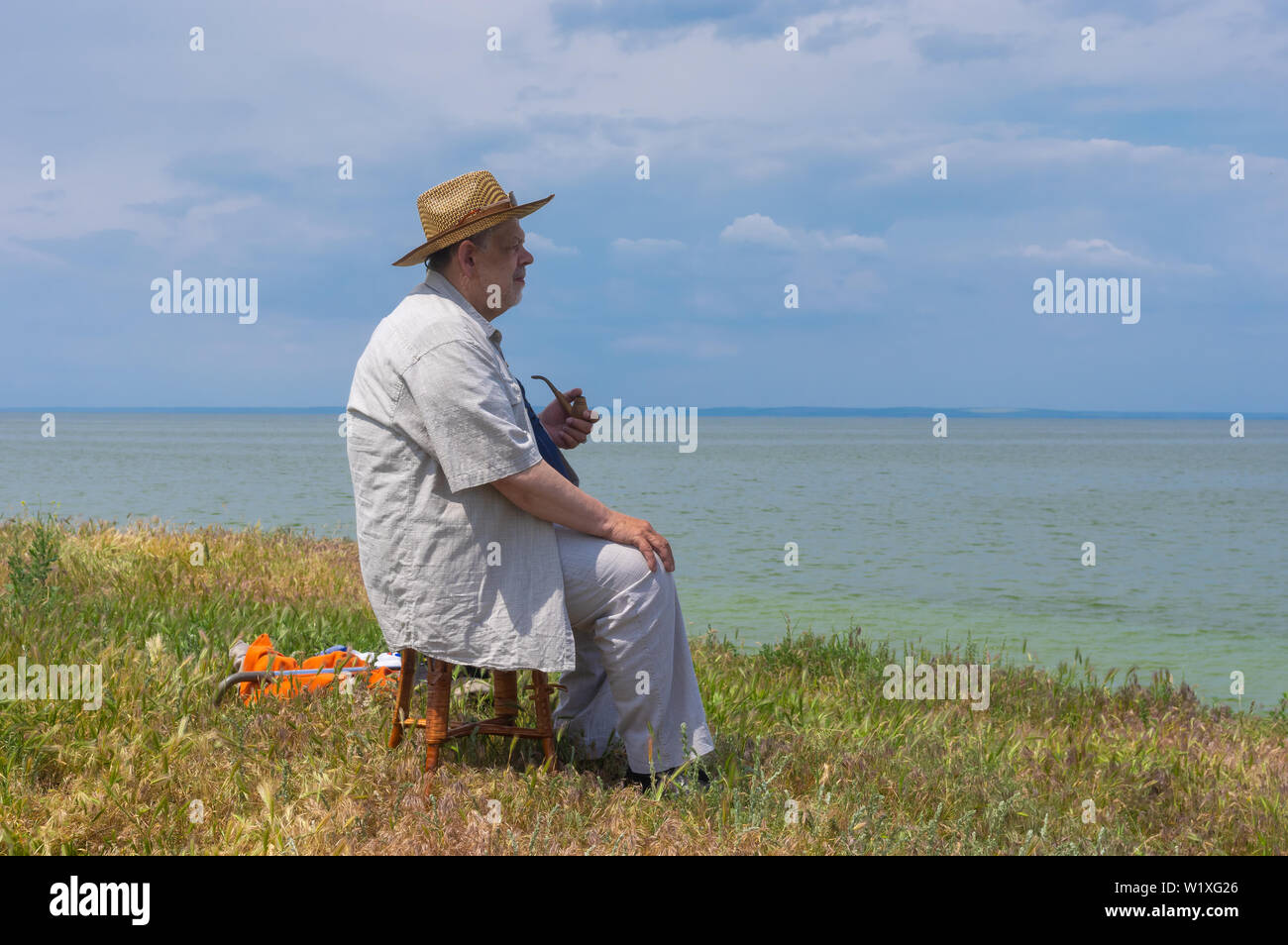 Lonely senior man sitting on a stool on abrupt riverside of the Dnipro river, Ukraine Stock Photo