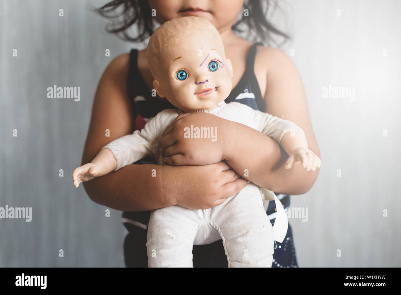 little asian girl hugging her favorite worn grimy doll. Concept of Lonely child, love, childhood and parenting. Selective focus on the doll. Stock Photo