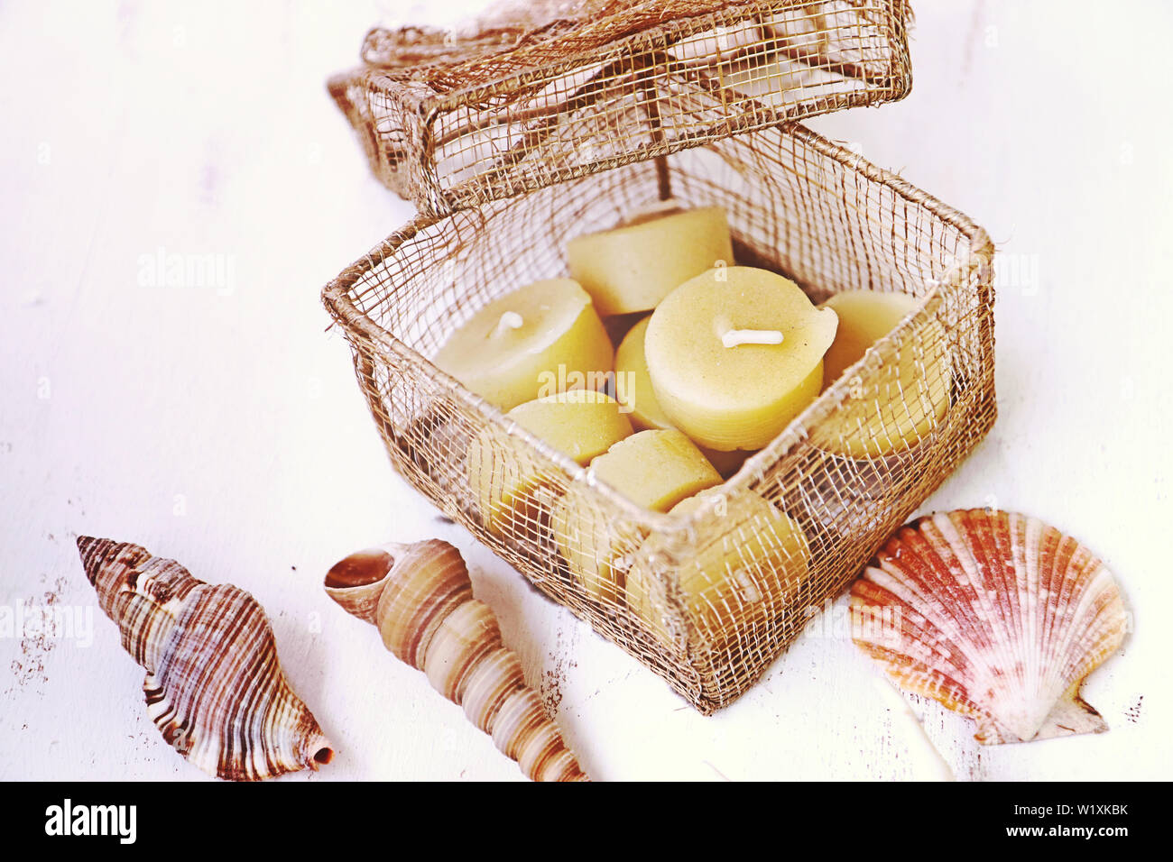 Still life: beeswax candles in a gold wire mesh box with sea shells on a white wooden table, top view Stock Photo