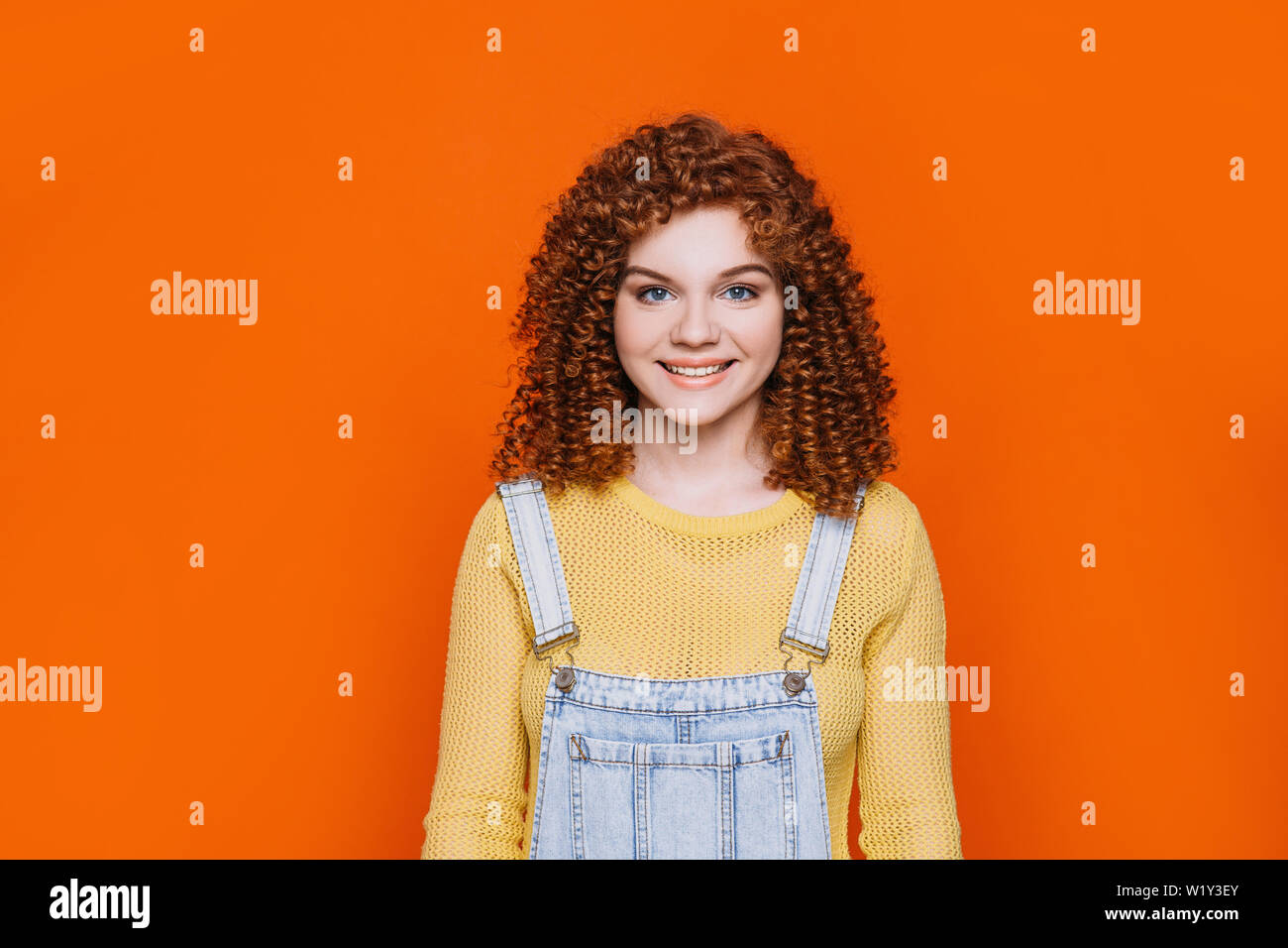 Curly- haired funny woman smiling and looking at camera on orange background Stock Photo