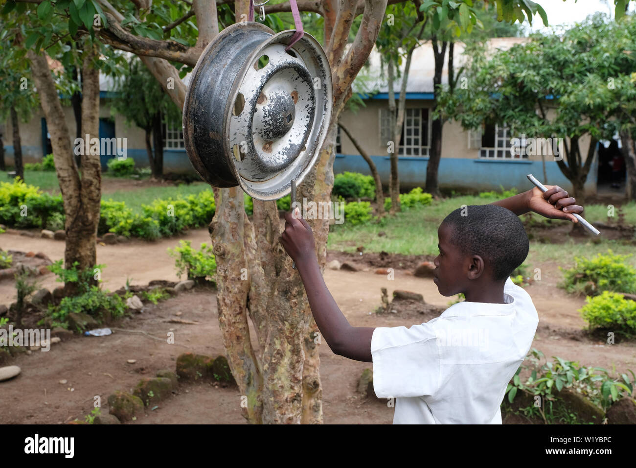 Boy beats a car rim, car wheel, as a bell at the Itiji Primary School in Mbeya, Tanzania. Stock Photo