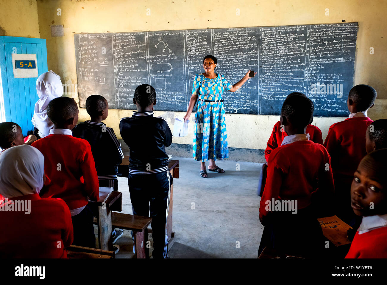 Teacher and students in red school uniforms in a school class of the Mwenge Primary School in Mbeya, Tanzania Stock Photo
