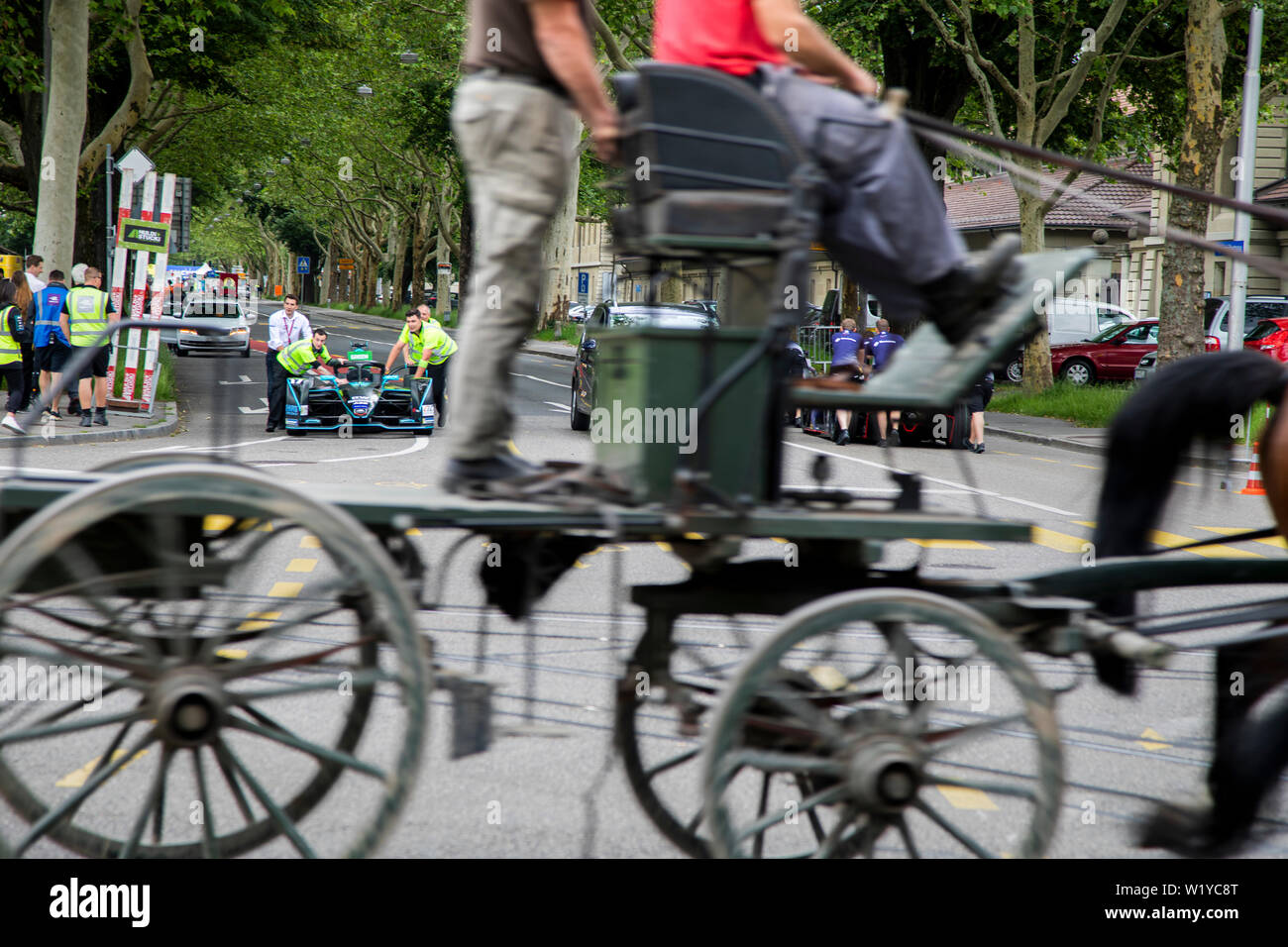 A horse caddy speeds past while crew members push one of the HWA Formula E cars from the pitlane back to the garage ahead of the  ABB FIA Formula E race in Bern. Stock Photo