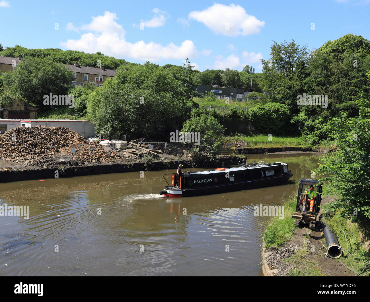 Canal narrow boat “Harlequin” makes a tight turn as it passes Finsley Gate wharf  on the Leeds and Liverpool canal in Burnley on a sunny day. Stock Photo