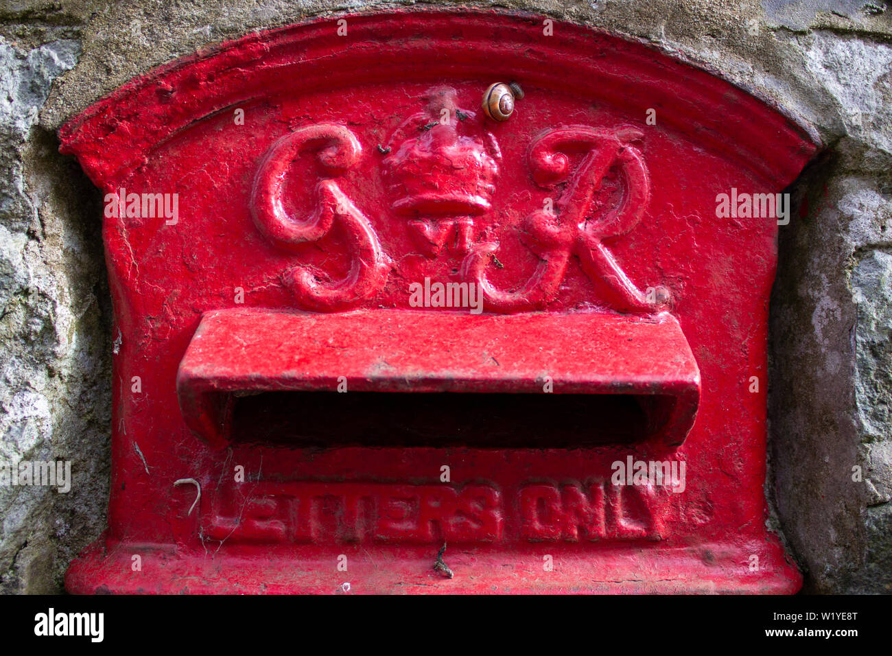 A snail crawling across an old Royal Mail postbox, set in a wall Stock Photo