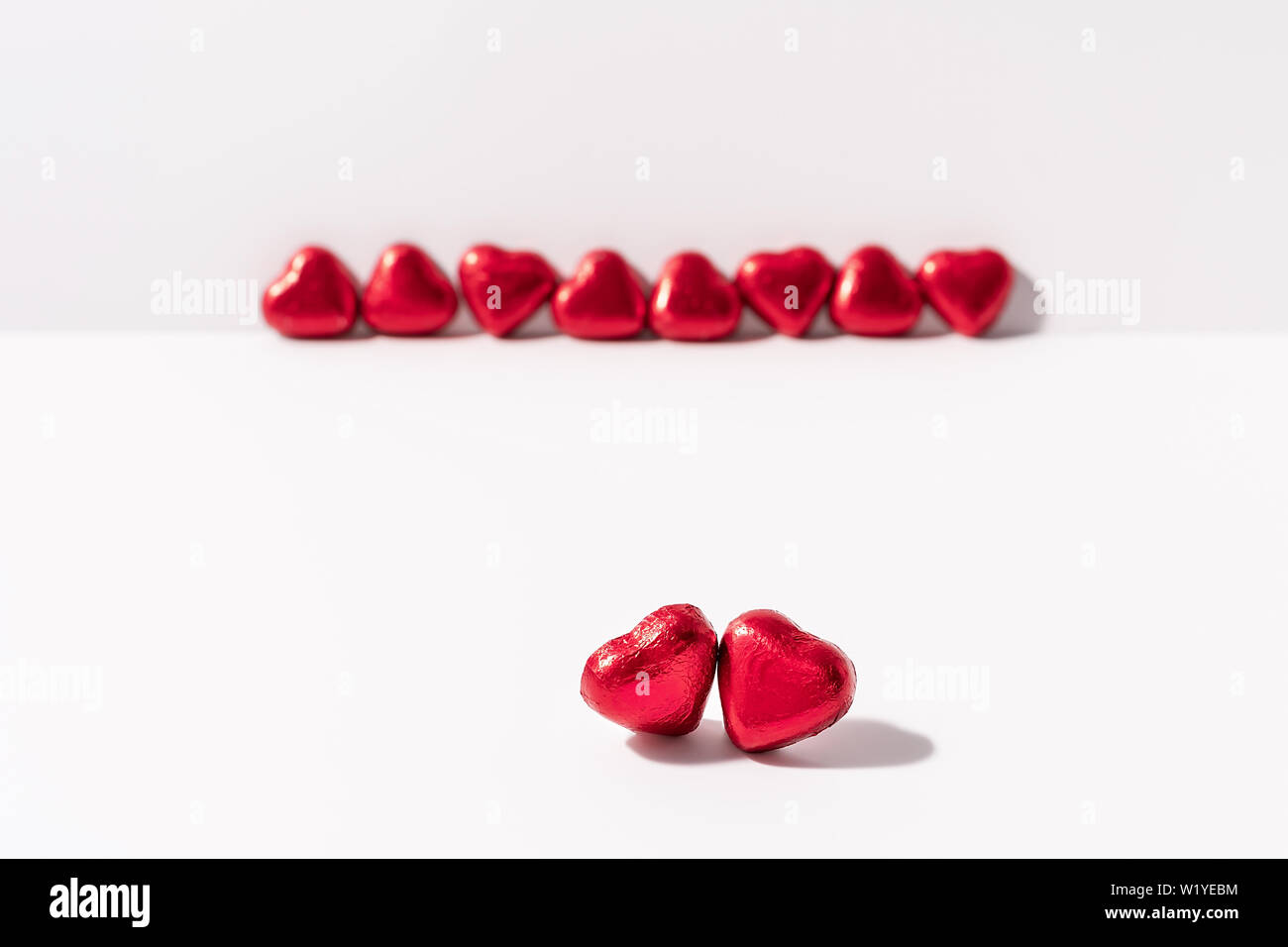 Heart shape chocolates wrapped in red foil on white background. Valentines day gift. Love and parting concept. Copy space. Stock Photo