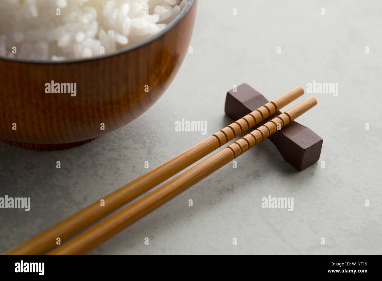 Traditional Japanese wooden chopsticks and a bowl with white rice in the background Stock Photo