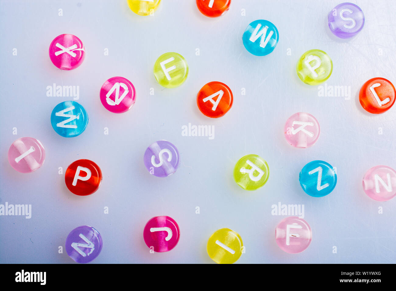Multi color alphabet letter beads placed randomly on white background