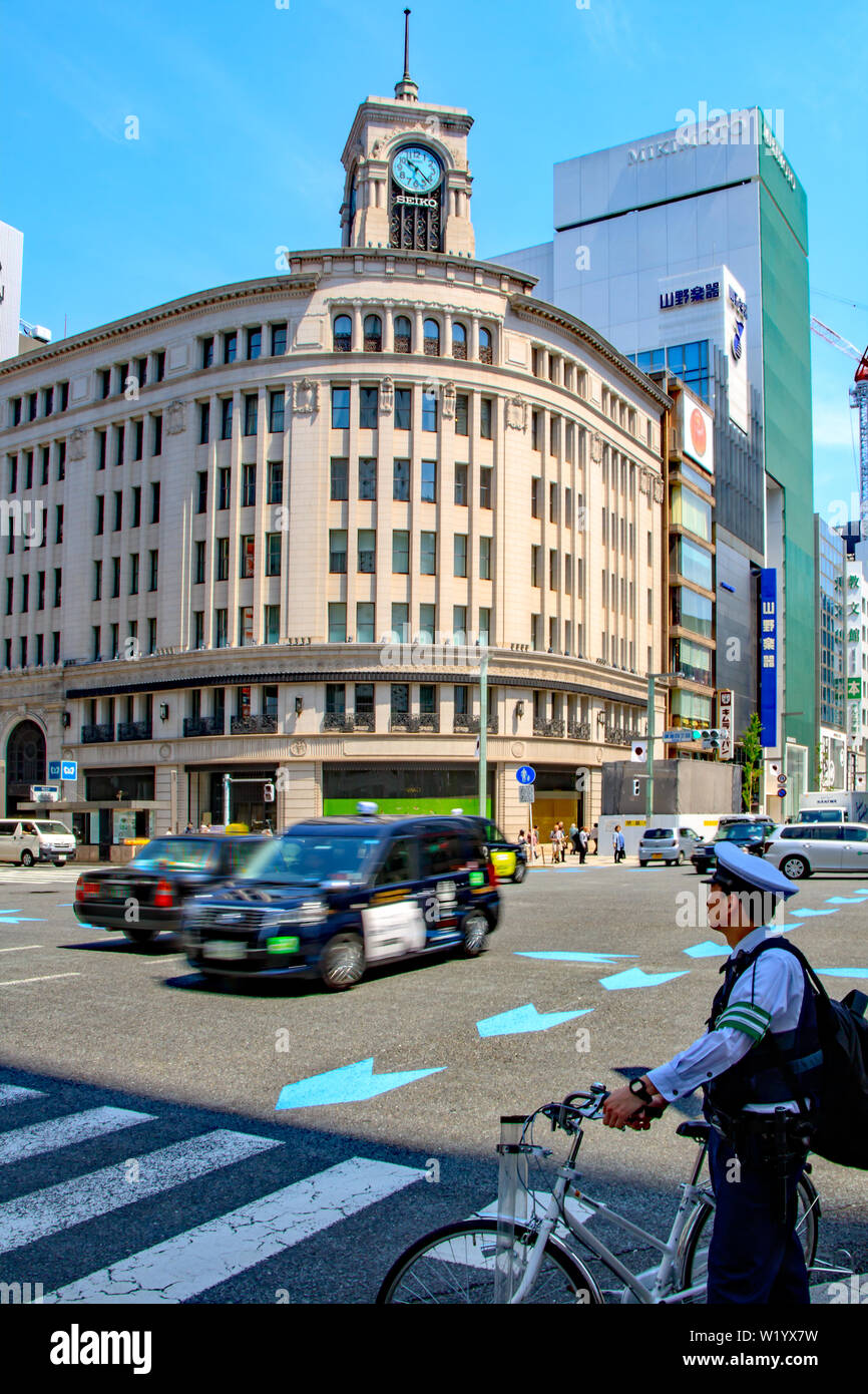 A policeman waits to cross at the Ginza Yonchome crossing Tokyo, Japan with Wako Department Store and its iconic clock tower in the background Stock Photo