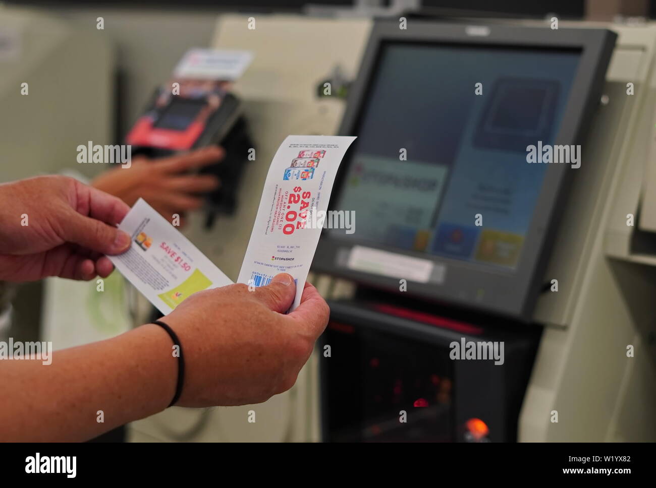 Cromwell, CT / USA - June 16, 2019: Tanned hands holding coupons up in front of a self checkout kiosk Stock Photo