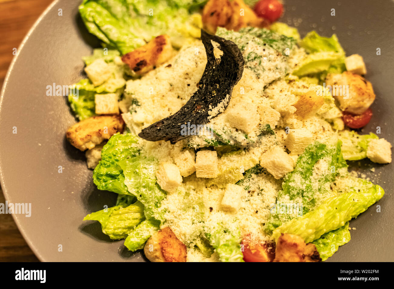 Healthy Caesar salad in brown plate on dark wooden table with Shallow depth of focus over dark grunge background Stock Photo