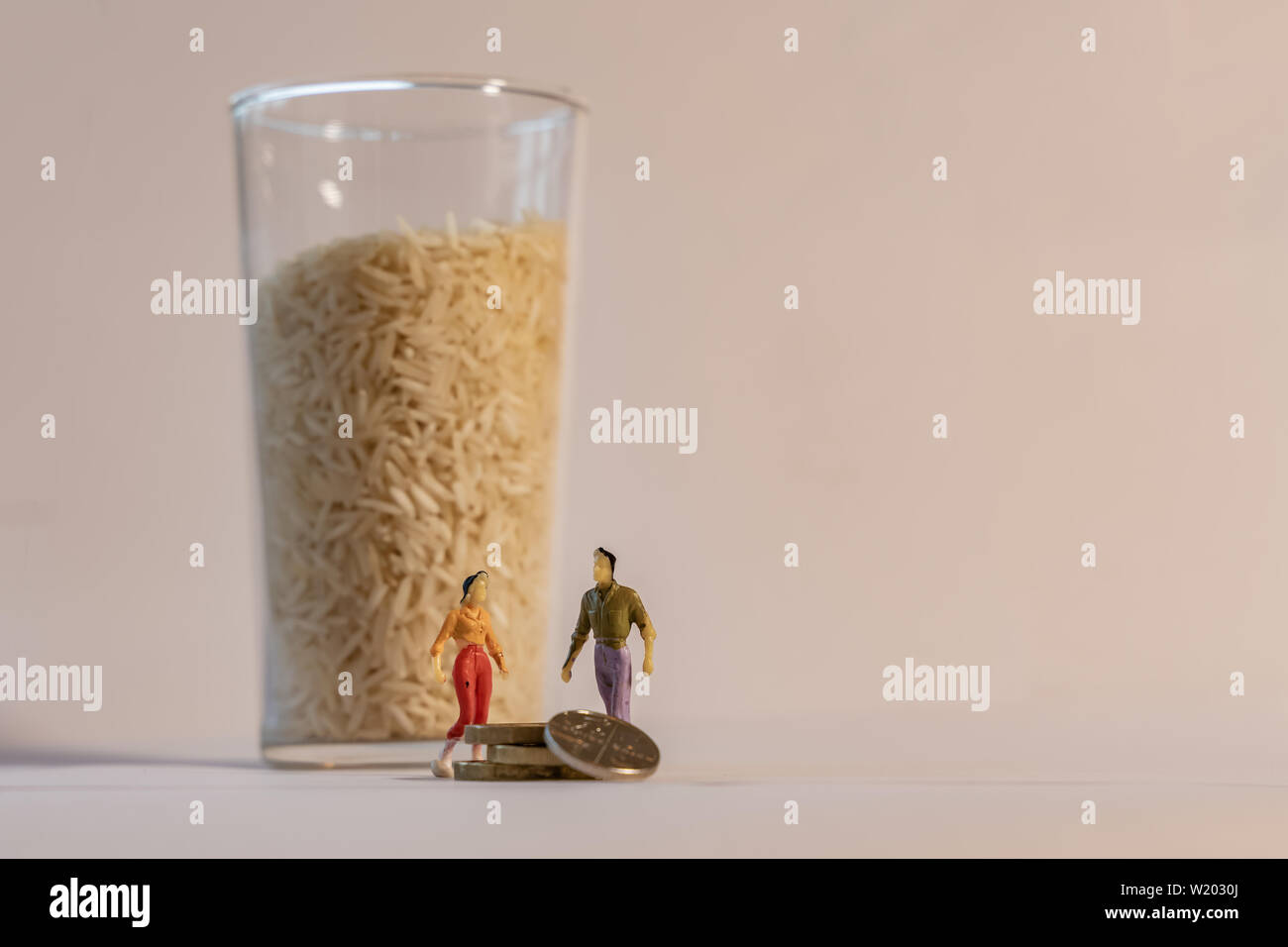 Miniature woman and man figure standing next to big glass of rice and counting coins. Shallow depth of field background. Family budget, healthy lifest Stock Photo