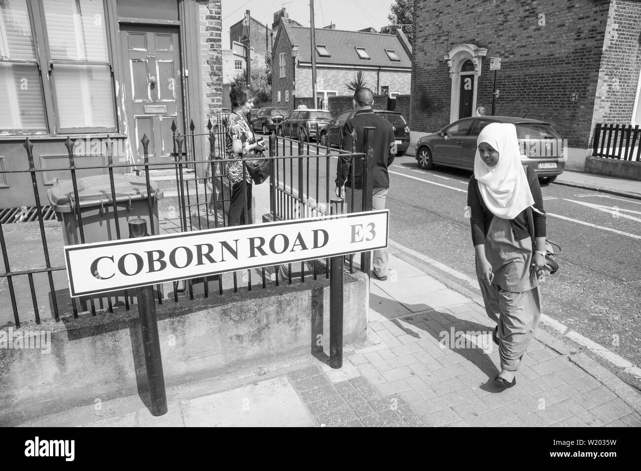 LONDON ENGLAND - JULY 13 2013; Woman in hajib walks around street corner of Coborn Road past the road sign in monochrome. Stock Photo