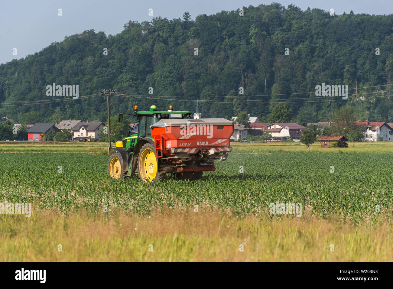 John Deere tractor with red tank in the back spraying on a field Stock Photo